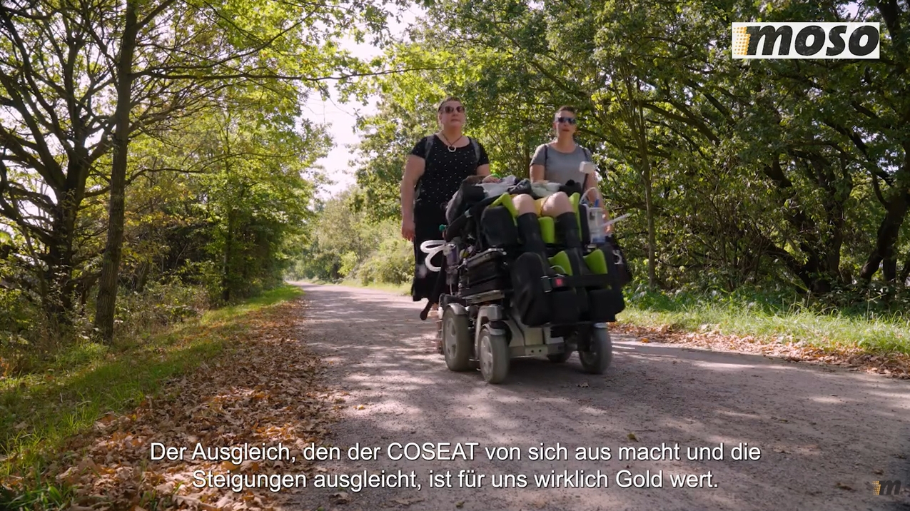 Zwei Frauen unterwegs mit einem Kind, das im COSEAT liegt. Eine der Frauen sagt: "Der Ausgleich, den der COSEAT von sich aus macht und die Steigungen ausgleicht, ist für uns wirklich Gold wert."