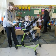 Ein Kind im EasyStand Zing in 20° zurück geneigter Position wird von einer Erzieherin in einer Schule angeschoben.