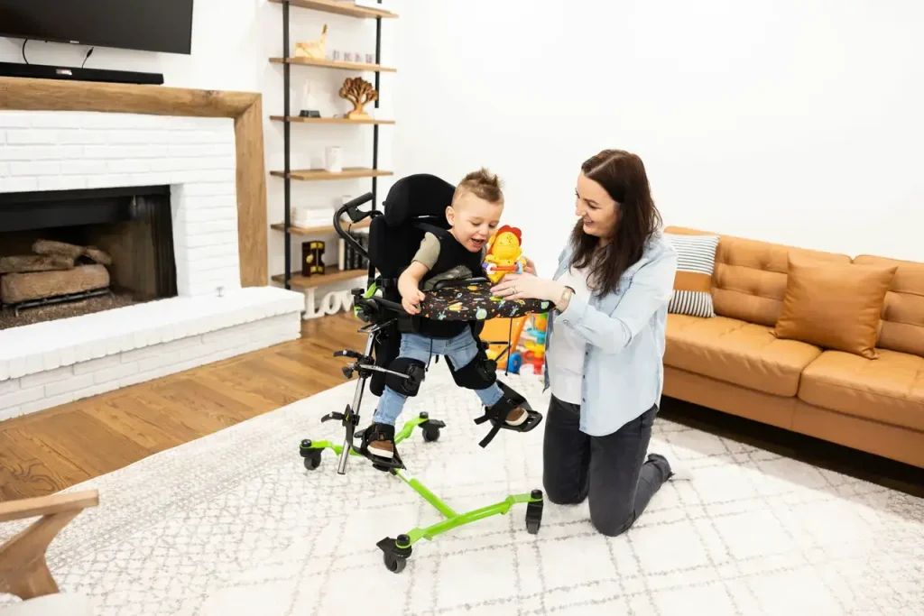 Ein Junge im Zing in aufrechter Position, der mit seiner Mutter spielt. Seine Beine werden seitlich abgespreizt gehalten. 