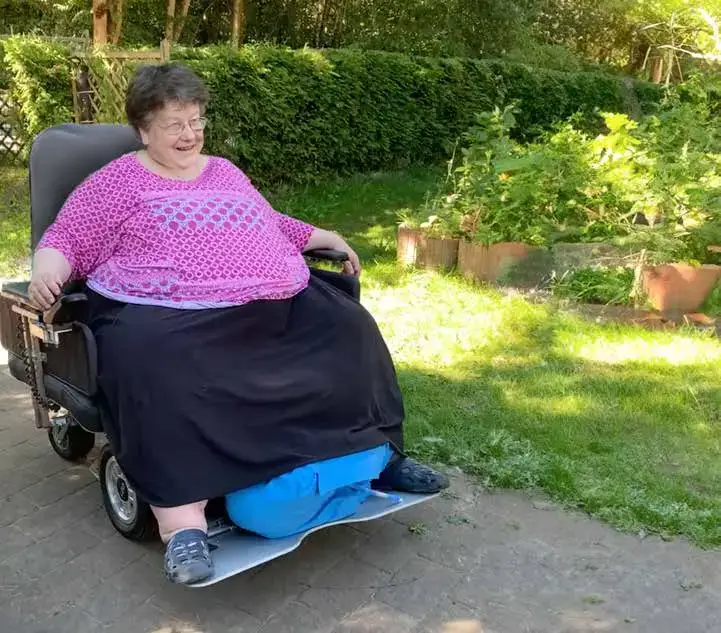 Eine Frau, die mit dem LEOplus in einem Park fährt. Bei diesem Sonderbau gibt es eine breitere Fläche für Sitz- und Rückenpolster, sowie ein breiteres Fußbrett.