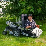 Der LEOlevel Rollstuhl mit aktiver Liftfunktion, seitlich fotografiert auf einer Wiese unter Bäumen.